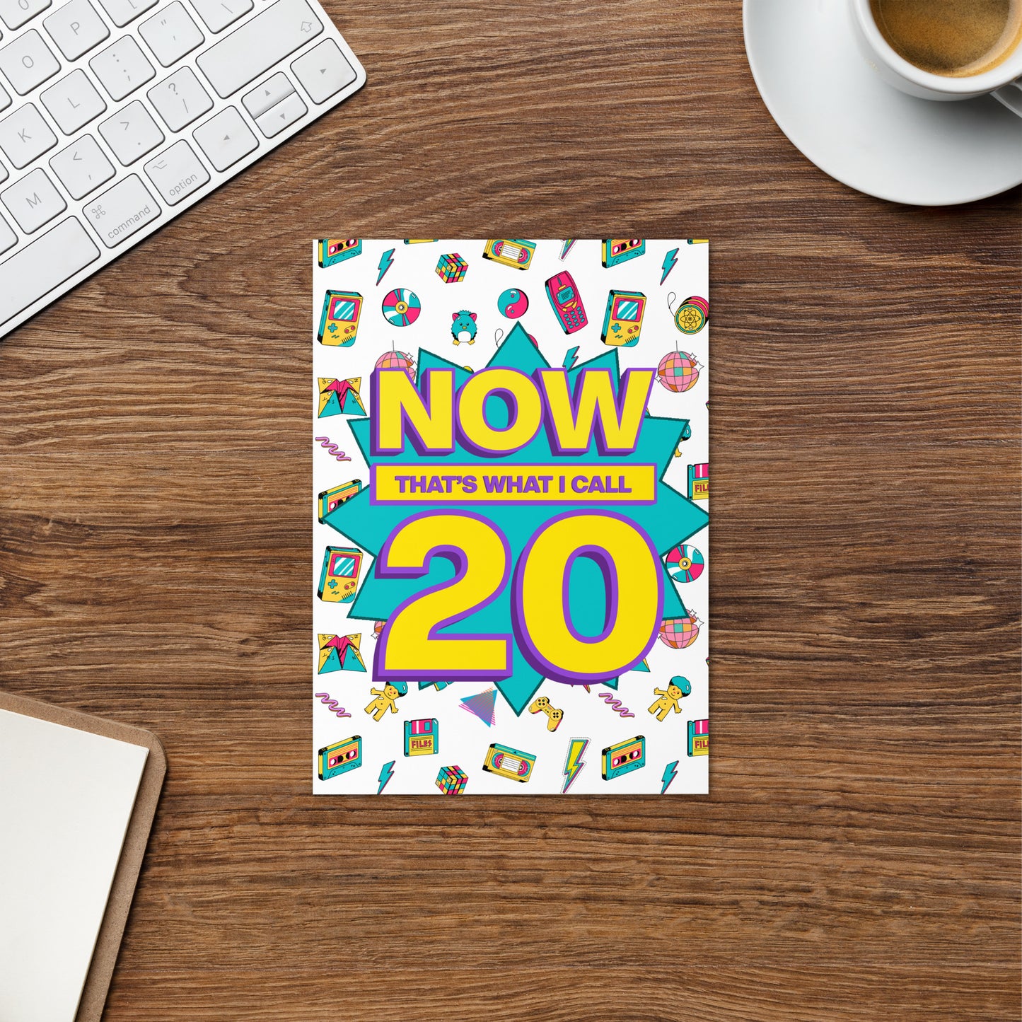 Colourful greetings card titled 'Now That's What I Call 20' on a wooden desk with a keyboard and coffee cup. Mock of now that’s what I call old. Funny greetings card for 20th birthday.