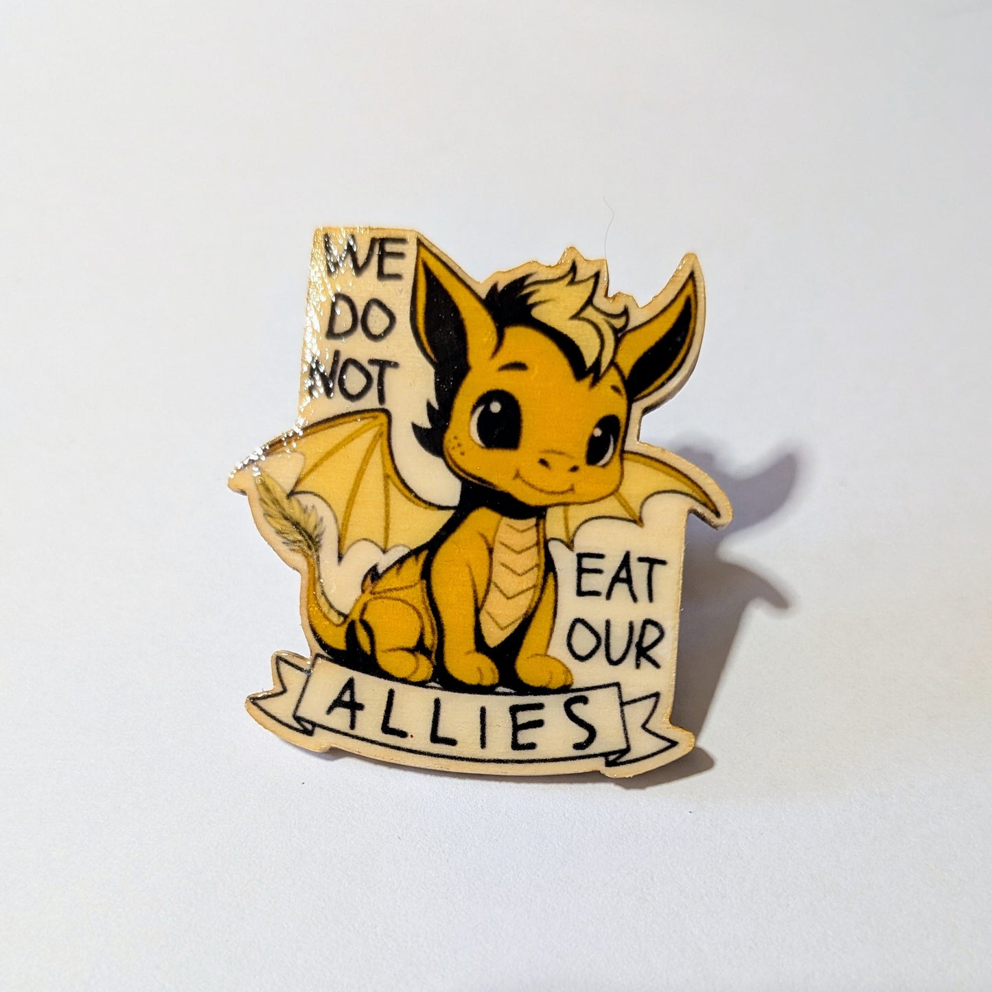 Andarna The Golden Dragon pin with text 'We do not eat our allies' on a white background. From Rebecca Yarros series Fourth Wing. Feathertail dragon